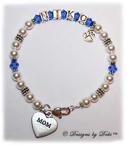 Designs by Debi Handmade Jewelry Pet Name Keepsake Bracelet in the the Kiara Style Pearls bead combination with Sapphire (September) crystals, a heart padlock lobster clasp, Mom heart charm and additional Paw charm at the end of the name. Mother's Bracelet Doggie Mom Bracelet