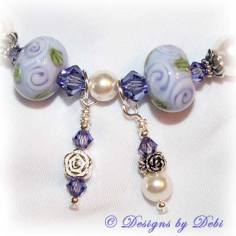 Designs by Debi Jewelry for Charity Piece for May 2010 to raise money for The Cystic Fibrosis Foundation. A one-of-a-kind artisan handmade bracelet with round handmade glass beads adorned with purple roses and green leaves, swarovski crystal tanzanite bicones, white swarovski pearls, sterling silver rose beads, sterling silver rose spacer beads and a sterling silver roses toggle clasp. OOAK