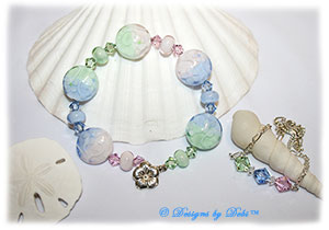 Designs by Debi Handmade Jewelry Aloha Collection Bangle Bracelet and Anklet Set. Features a set of handmade lampwork floral spree beads with a pstel gradient pattern in pink, light blue and mint green, accent beads and swarovski crystal bicones in rosaline, light sapphire and chrysolite with a sterling silver flower clasp and anklet with matching crystals.