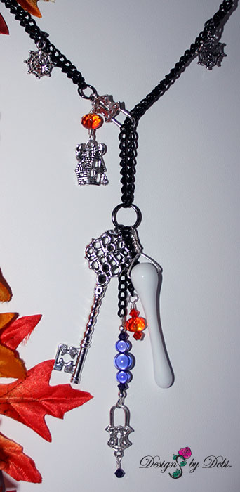 Center and dangles of Designs by Debi Handmade Jewelry for Charity Set October 2012 to benefit Born This Way Foundation. A one of a kind Halloween theme lariat necklace and earrings made with Swarovksi and other crystals in black, black diamond, fire opal and purple velvet, a unique Haunted House focal piece, black curb chain, a white glass ghost, haunted house, spider web and padlock charms, a white glass bone pendant bead and a large silver skeleton key. Copyright Designs by Debi.