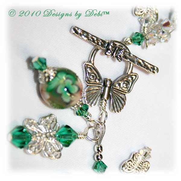 Spring Butterflies One-of-a-Kind Handmade Bracelet made with artisan handmade polymer clay round beads with green and white flowers and green butterflies, sterling silver butterflies, Swarovski crystal butterflies and Swarovski crystal AB and light emerald bicones with a sterling silver butterfly toggle style clasp. Close-up.