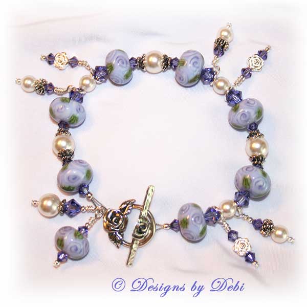 Designs by Debi Jewelry for Charity Piece for May 2010 to raise money for The Cystic Fibrosis Foundation. A one-of-a-kind artisan handmade bracelet with round handmade glass beads adorned with purple roses and green leaves, swarovski crystal tanzanite bicones, white swarovski pearls, sterling silver rose beads, sterling silver rose spacer beads and a sterling silver roses toggle clasp. OOAK