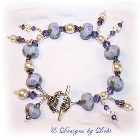 Designs by Debi Jewelry for Charity Piece for May 2010 to raise money for The Cystic Fibrosis Foundation. A one-of-a-kind artisan handmade bracelet with round handmade glass beads adorned with purple roses and green leaves, swarovski crystal tanzanite bicones, white swarovski pearls, sterling silver rose beads, sterling silver rose spacer beads and a sterling silver roses toggle clasp. OOAK