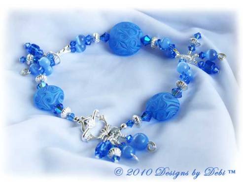 Designs by Debi Jewelry for Charity Piece for April 2010 to raise money for Autism Speaks. A one-of-a-kind artisan handmade bracelet with etched handmade glass lentil beads in a swirled pattern of shades of blue and a hint of violet, swarovski crystal sapphire and sapphire ab2x bicones, sapphire blue cat's eye beads, blue glass barrels, sterling silver twisted double curve and saucer beads and an abstract sterling silver toggle clasp OOAK.