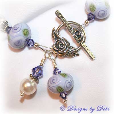 Designs by Debi Jewelry for Charity Piece for May 2010 to raise money for The Cystic Fibrosis Foundation. A one-of-a-kind artisan handmade bracelet with round handmade glass beads adorned with purple roses and green leaves, swarovski crystal tanzanite bicones, white swarovski pearls, sterling silver rose beads, sterling silver rose spacer beads and a sterling silver roses toggle clasp. OOAK