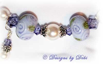 Designs by Debi Jewelry for Charity Piece for May 2010 to raise money for The Cystic Fibrosis Foundation. A one-of-a-kind artisan handmade bracelet with round handmade glass beads adorned with purple roses and green leaves, swarovski crystal tanzanite bicones, white swarovski pearls, sterling silver rose beads, sterling silver rose spacer beads and a sterling silver roses toggle clasp. OOAK