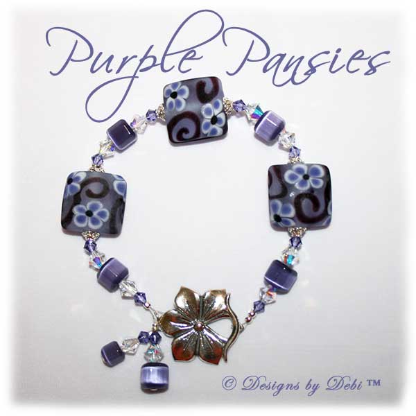 Designs by Debi Handmade Jewelry Purple Pansies one of a kind ooak handmade tanzanite purple lampwork and crystal bracelet made in honor of national alzheimer's disease awareness month to raise money for the Alzheimer's Association. It was made with purple flowers on pale lavender handmade square lampwork beads with amethyst scrolls, purple cat's eye beads, crystal ab and tanzanite crystals and sterling silver with a pansy flower toggle clasp.