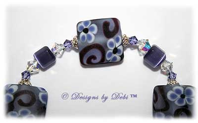 Designs by Debi Handmade Jewelry Purple Pansies one of a kind ooak handmade tanzanite purple lampwork and crystal bracelet made in honor of national alzheimer's disease awareness month to raise money for the Alzheimer's Association. It was made with purple flowers on pale lavender handmade square lampwork beads with amethyst scrolls, purple cat's eye beads, crystal ab and tanzanite crystals and sterling silver with a pansy flower toggle clasp.