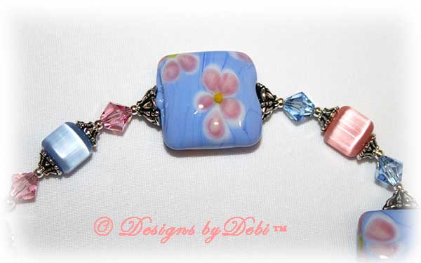 Designs by Debi Handmade Jewelry Sweet Angels one of a kind ooak handmade light pink and light blue lampwork and crystal bracelet made in honor of national pregnancy and infant loss awareness month to raise money for Missing GRACE Foundation. It was made with pink flowers on blue handmade square lampwork beads, pink and blue cat's eye beads, pink and blue crystals and sterling silver with a flower toggle clasp.