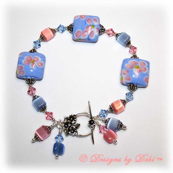 Designs by Debi Handmade Jewelry Sweet Angels one of a kind ooak handmade light pink and light blue lampwork and crystal bracelet made in honor of national pregnancy and infant loss awareness month to raise money for Missing GRACE Foundation. It was made with pink flowers on blue handmade square lampwork beads, pink and blue cat's eye beads, pink and blue crystals and sterling silver with a flower toggle clasp.