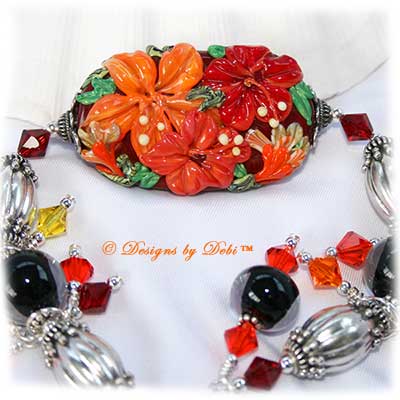 Designs by Debi Handmade Jewelry for Charity Piece for September 2010 to raise money for Stand Up To Cancer. A one-of-a-kind artisan handmade bracelet with an oblong hibiscus focal in reds and oranges, clear-encased black handmade glass beads, bali sterling silver fluted granulated oval beads, swarovski crystal siam red, hyacinth orange, sun light orange and citrine yellow bicones, bali sterling silver spacer beads, sterling silver seamless round beads, two large dangles and a bali sterling silver granulated detail toggle clasp. OOAK one of a kind