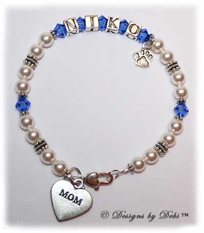 Designs by Debi Handmade Jewelry Kiara Style Pet Keepsake Bracelet in the Pearls bead combination with Sapphire (September) crystals, a heart padlock lobster clasp, Mom heart charm and additional Paw charm added at the end of the name.