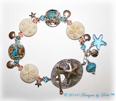 Designs by Debi Jewelry for Charity Piece for July 2010 to raise money for The Deepwater Horizon Memorial Fund. A one-of-a-kind artisan handmade bracelet with blue and beige lentil-shaped ocean within handmade glass beads, handmade glass sand dollar beads, swarovski crystal aquamarine and light peach bicones, sterling silver round beads, sterling silver sand dollar charms, sterling silver shell charms, sterling silver starfish charms, a swarovski crystal aquamarine starfish and a shiana thai sterling silver sand dollar toggle clasp. OOAK