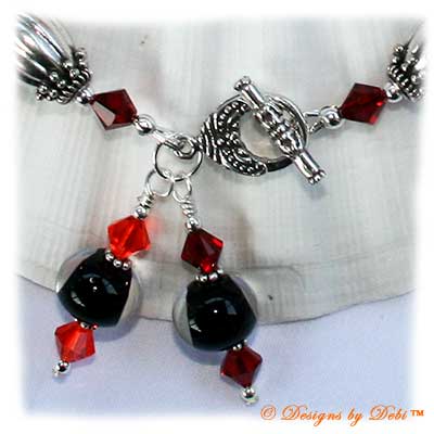 Designs by Debi Handmade Jewelry for Charity Piece for September 2010 to raise money for Stand Up To Cancer. A one-of-a-kind artisan handmade bracelet with an oblong hibiscus focal in reds and oranges, clear-encased black handmade glass beads, bali sterling silver fluted granulated oval beads, swarovski crystal siam red, hyacinth orange, sun light orange and citrine yellow bicones, bali sterling silver spacer beads, sterling silver seamless round beads, two large dangles and a bali sterling silver granulated detail toggle clasp. OOAK one of a kind