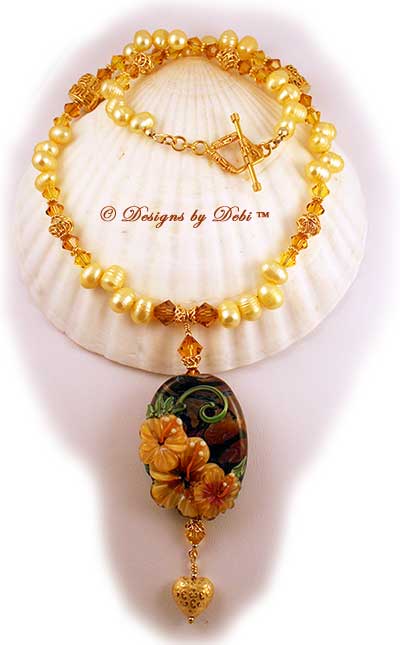 Designs by Debi September 2011 Jewelry for Charity Necklace Hawaiian Sunshine. A one of a kind necklace with a golden hibiscus handmade lampwork focal bead; golden yellow, dancing freshwater pearls, Bali vermeil squiggle pillows, filigree bicones and bead caps, daisy spacers, diamond-shaped toggle clasp and puffy heart dangle, and Swarovski crystal bicones in topaz and light topaz. One-of-a-kind OOAK